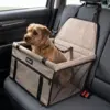 Lille brun hund sidder i et beige autostol til hunde fastgjort på bilens bagsæde.